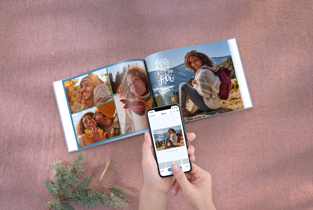 Pixum Fotobuch, vor dem zwei Hände ein Smartphone mit der Pixum App halten