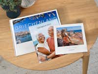 Fotobücher in der Pixum App gestalten Drei Fotobücher mit kreativen Urlaubsfotos liegen übereinander gestapelt auf einem Tisch. Sie sind unterschiedlich gross und bunt gestaltet.