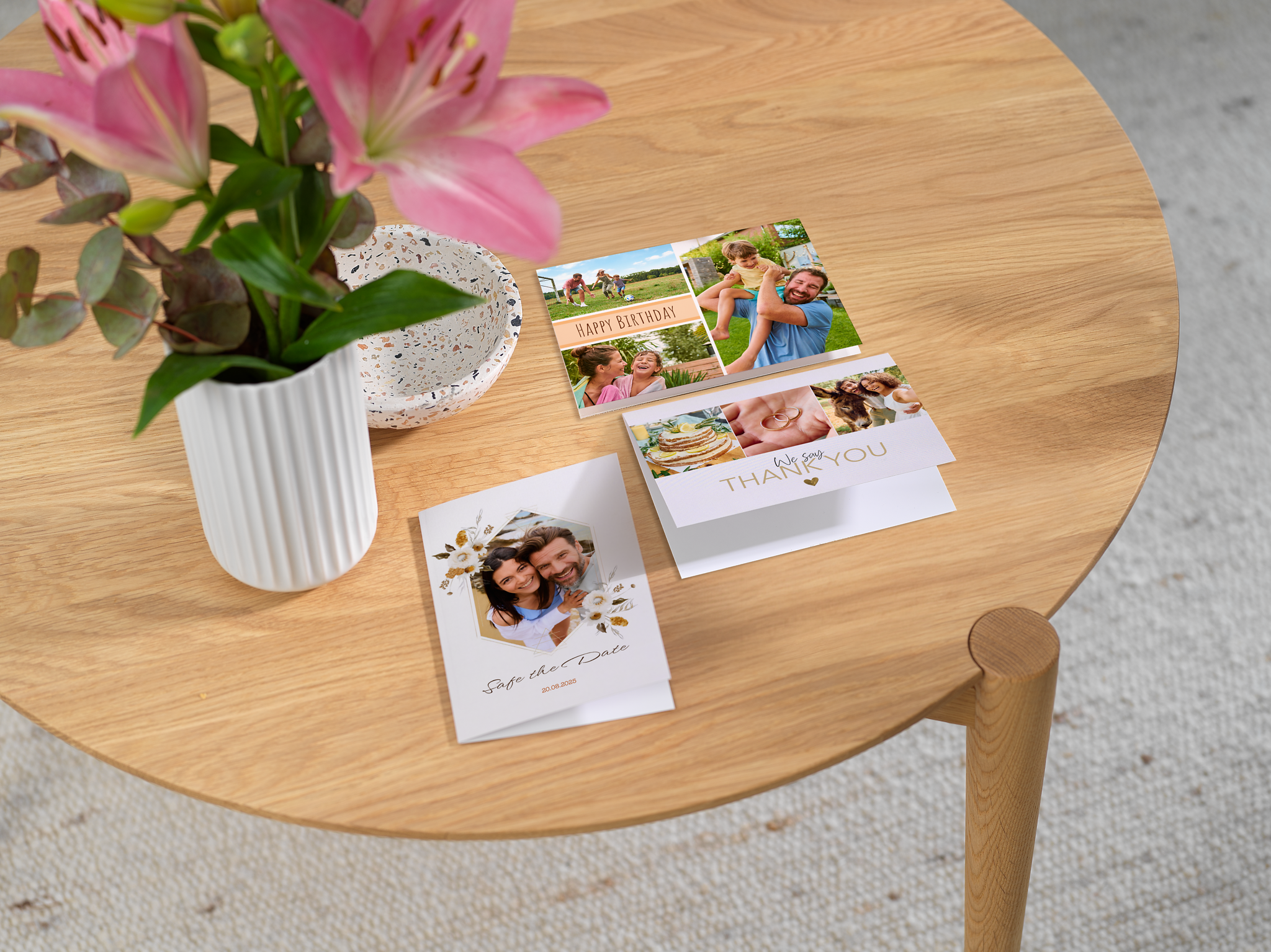 Sobre una mesa redonda de madera hay varias tarjetas fotográficas personalizadas, entre ellas una tarjeta de cumpleaños, una tarjeta de agradecimiento y una invitación. Junto a las tarjetas hay un jarrón.