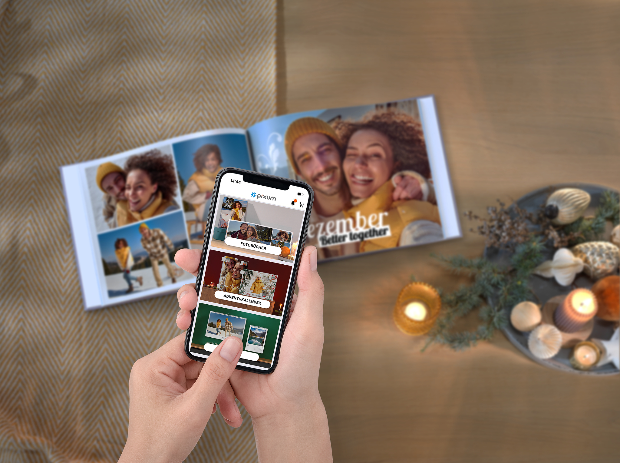 Pixum Fotobuch und ein Smartphone, auf dem die Pixum App zu sehen ist. Alles in einem weihnachtlichen Ambiente.