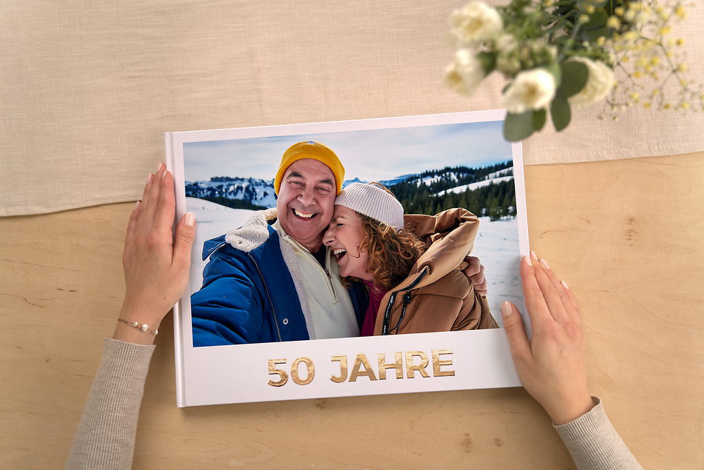 Hände halten ein Fotobuch zur goldenen Hochzeit mit dem Schriftzug „50 Jahre“ auf dem Deckblatt, ideal als persönliches Geschenk zum 50. Hochzeitstag