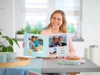 Bestellung bewerten Eine Frau, die ein aufgeschlagenes Pixum Fotobuch in die Kamera zeigt