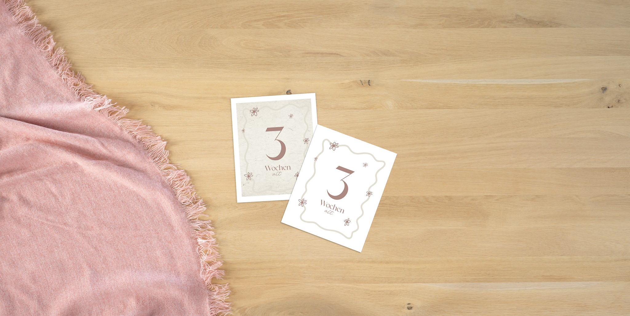 Auf einem Tisch liegen zwei Meilensteinkarten für die dritte Lebenswoche des Babys. Beide sind mit dem gleichen Design gestaltet. Die eine wurde zusätzlich durch einen passenden Hintergrund ergänzt.