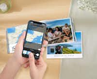 Álbum Digital Pixum en la app Manos con un smartphone en el que está abierta la aplicación Pixum. Al fondo hay un álbum de fotos Pixum con fotos de vacaciones y un mapa en las páginas.