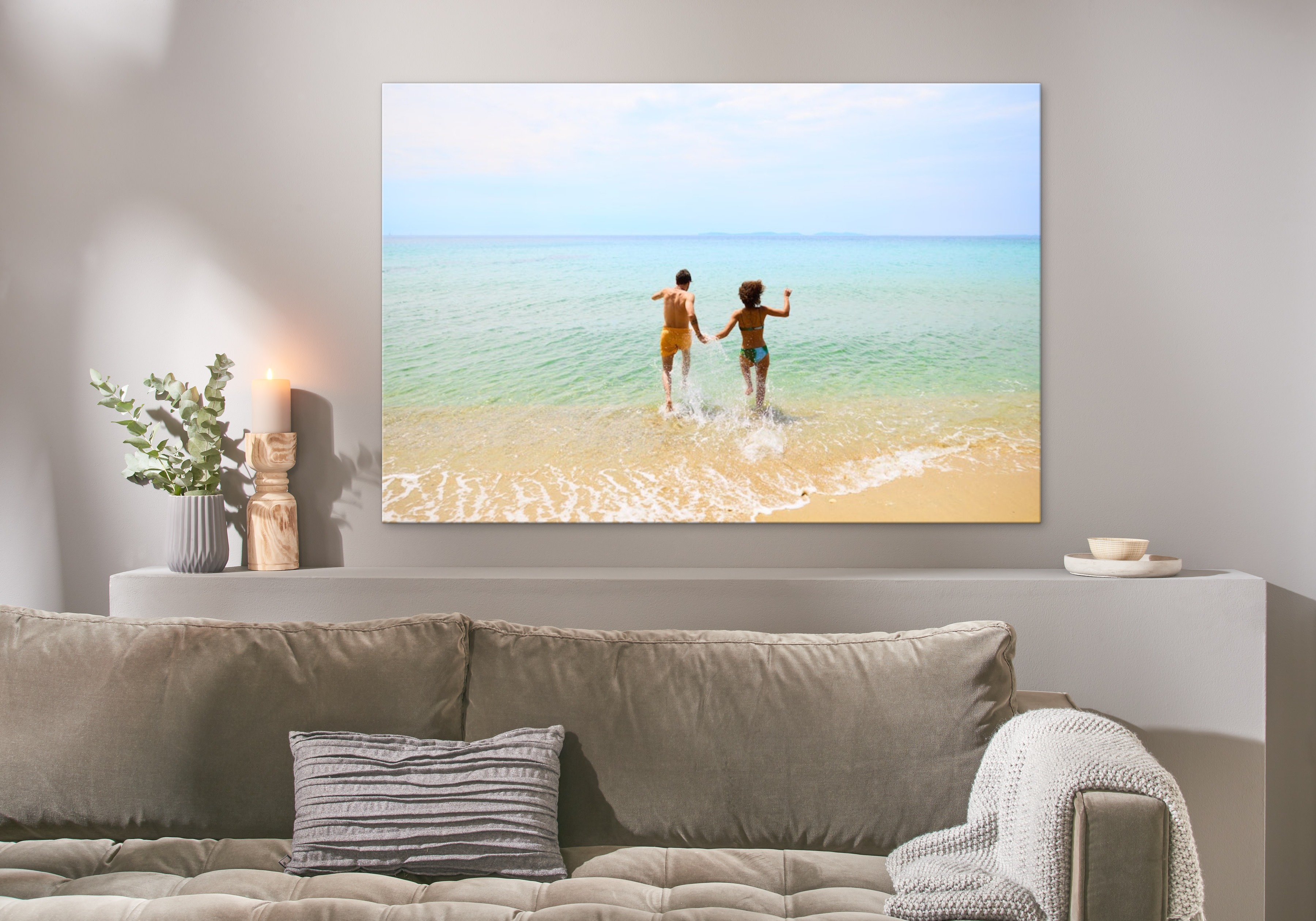Eine Fotoleinwand hängt über einem Sofa und zeigt ein Bild von einem Pärchen, dass ins Meer läuft.