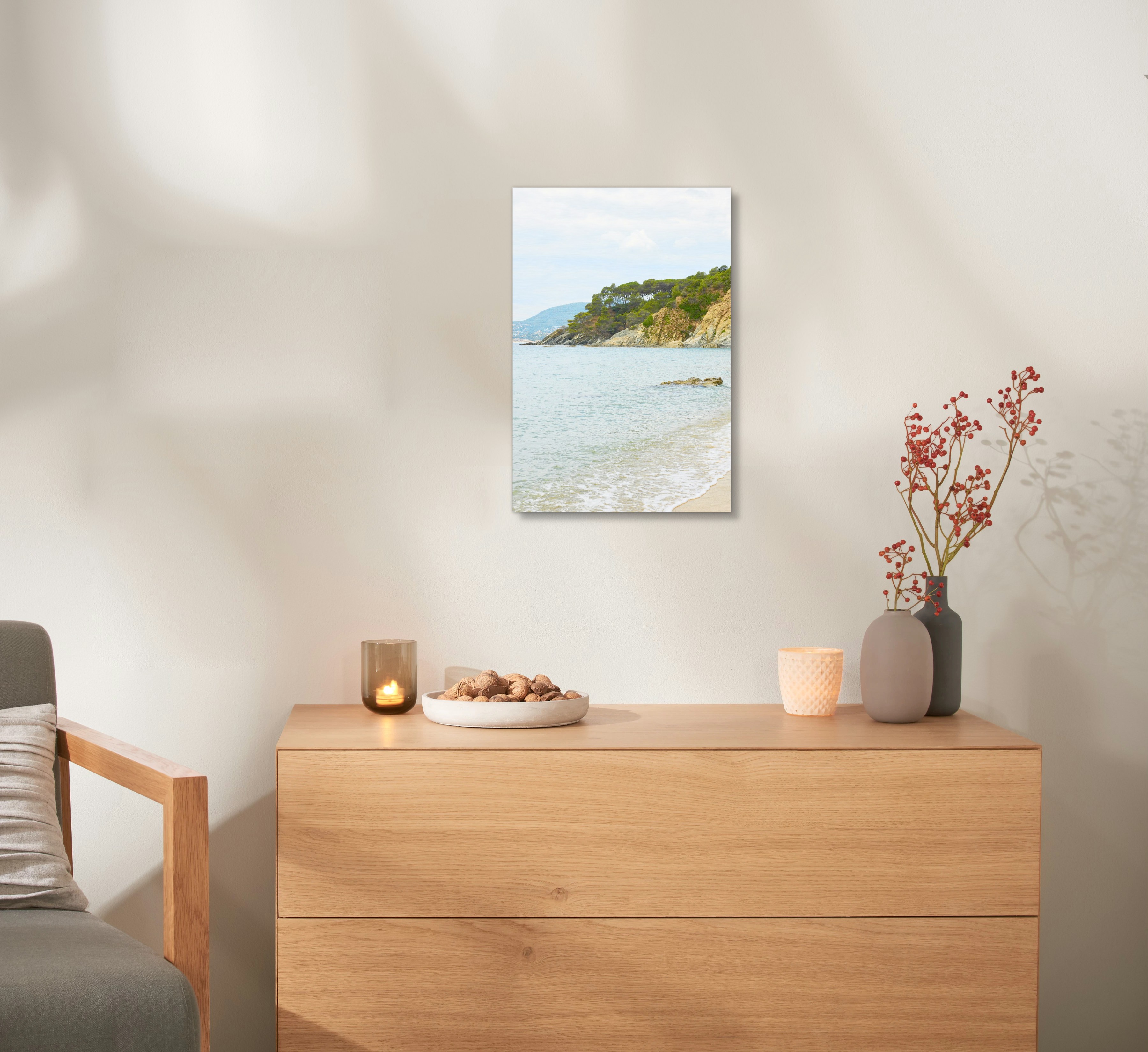 Ein Wandbild aus Holz mit einem Urlaubsfoto hängt an einer Wand, über einer Kommode. 