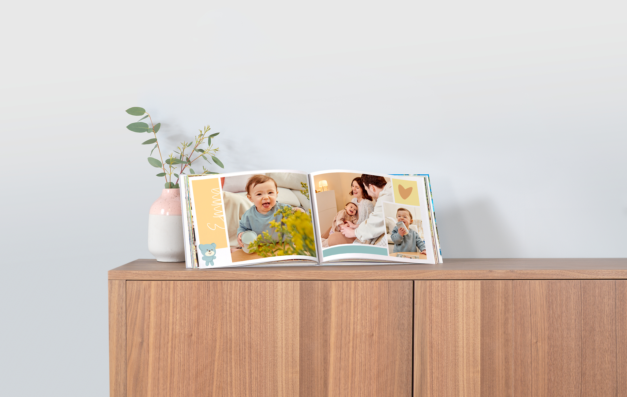 Auf einer Kommode steht ein Fotobuch, das als Babyalbum gestaltet worden ist. Die Seiten sind mit passenden Cliparts wie zum Beispiel kleinen Bärchen gestaltet.