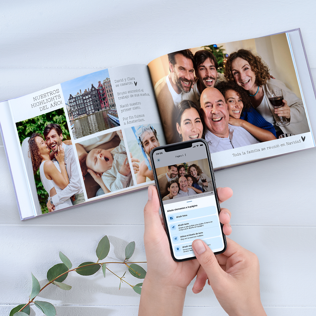 Álbum de fotos con texto abierto sobre una mesa y un móvil enseñando que se está haciendo en la app Pixum