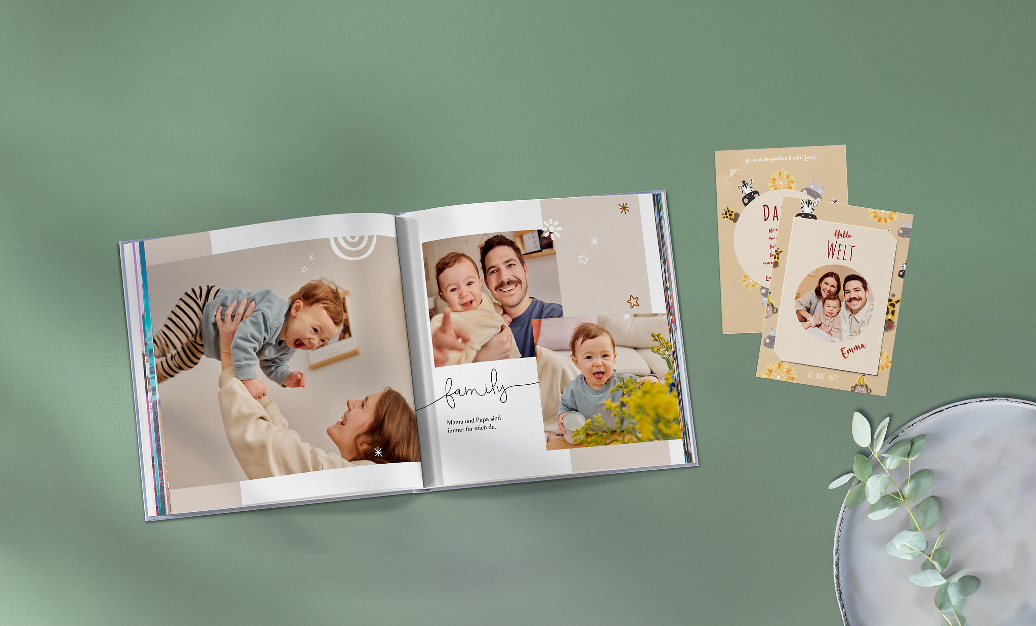 Pixum Fotobuch im quadratischen Format und Karte mit Einsteckfoto mit Baby- und Familienfotos auf einer grünen Unterlage
