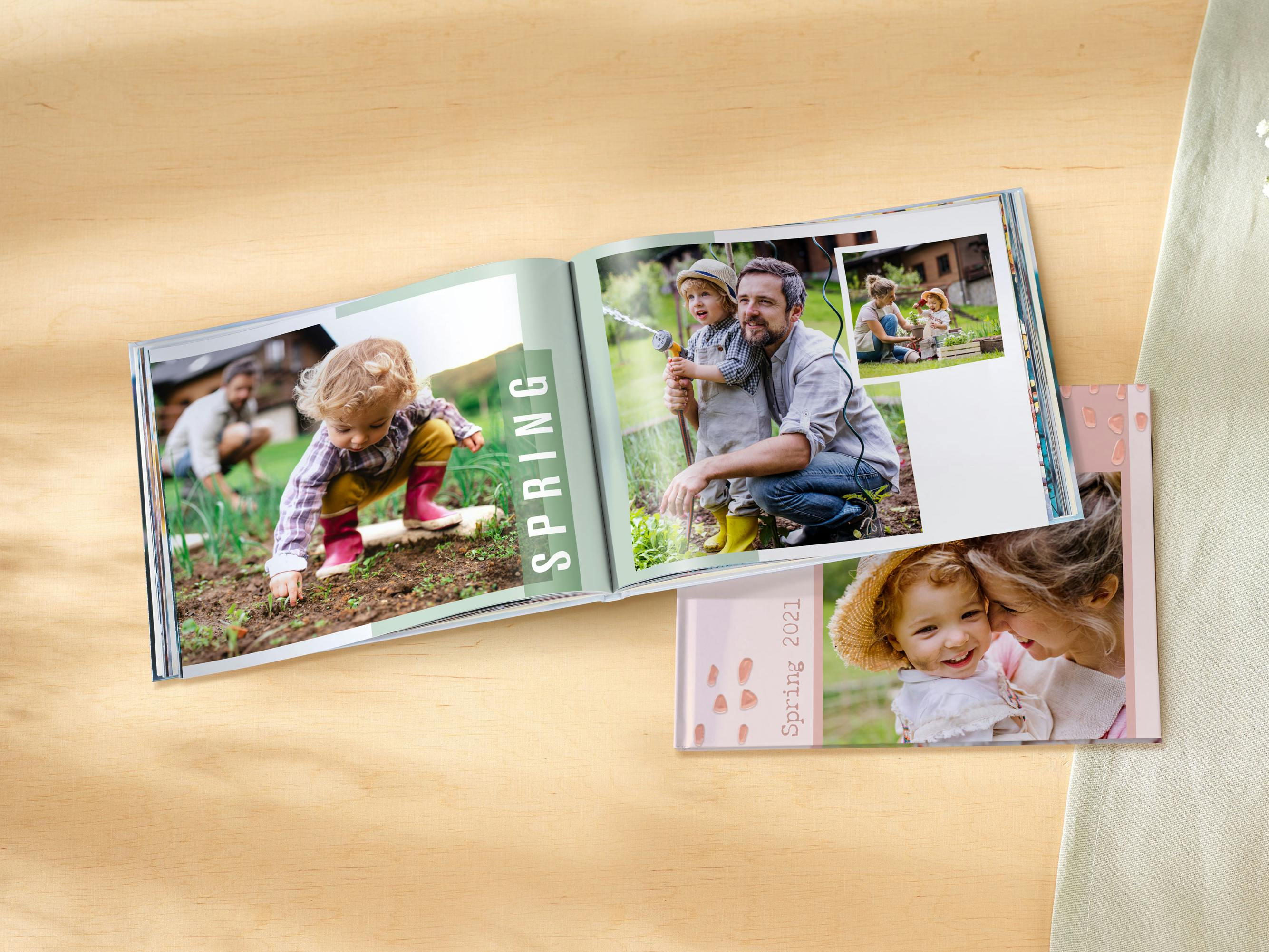 Aufgeschlagenes Fotobuch im Querformat mit frühlingshaften Familienfotos auf einem Holztisch mit hellgrauer Tischdecke