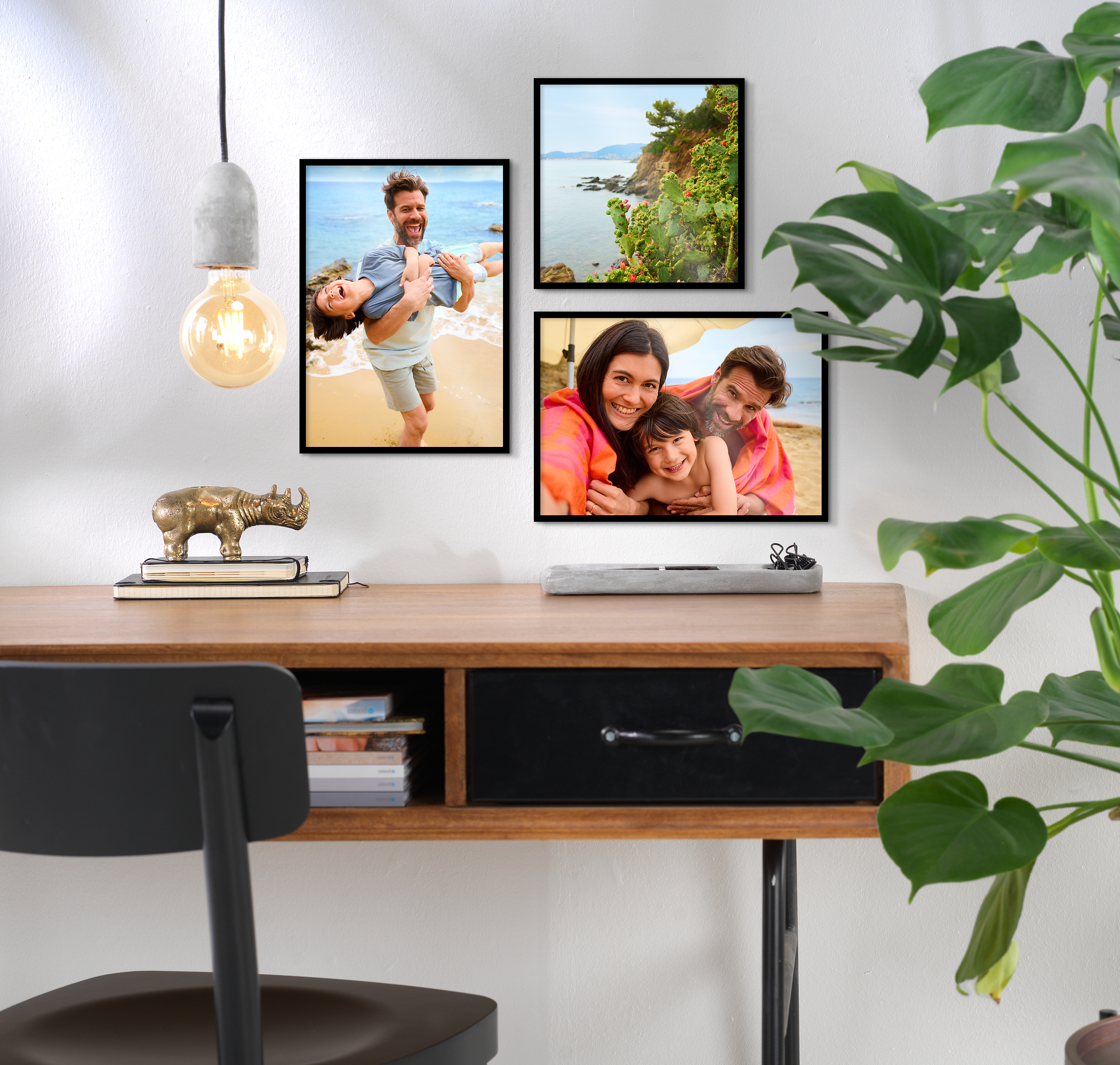 Das Bild zeigt eine Fotowand mit drei Bildern mit schwarzen Rahmen über einem Schreibtisch.