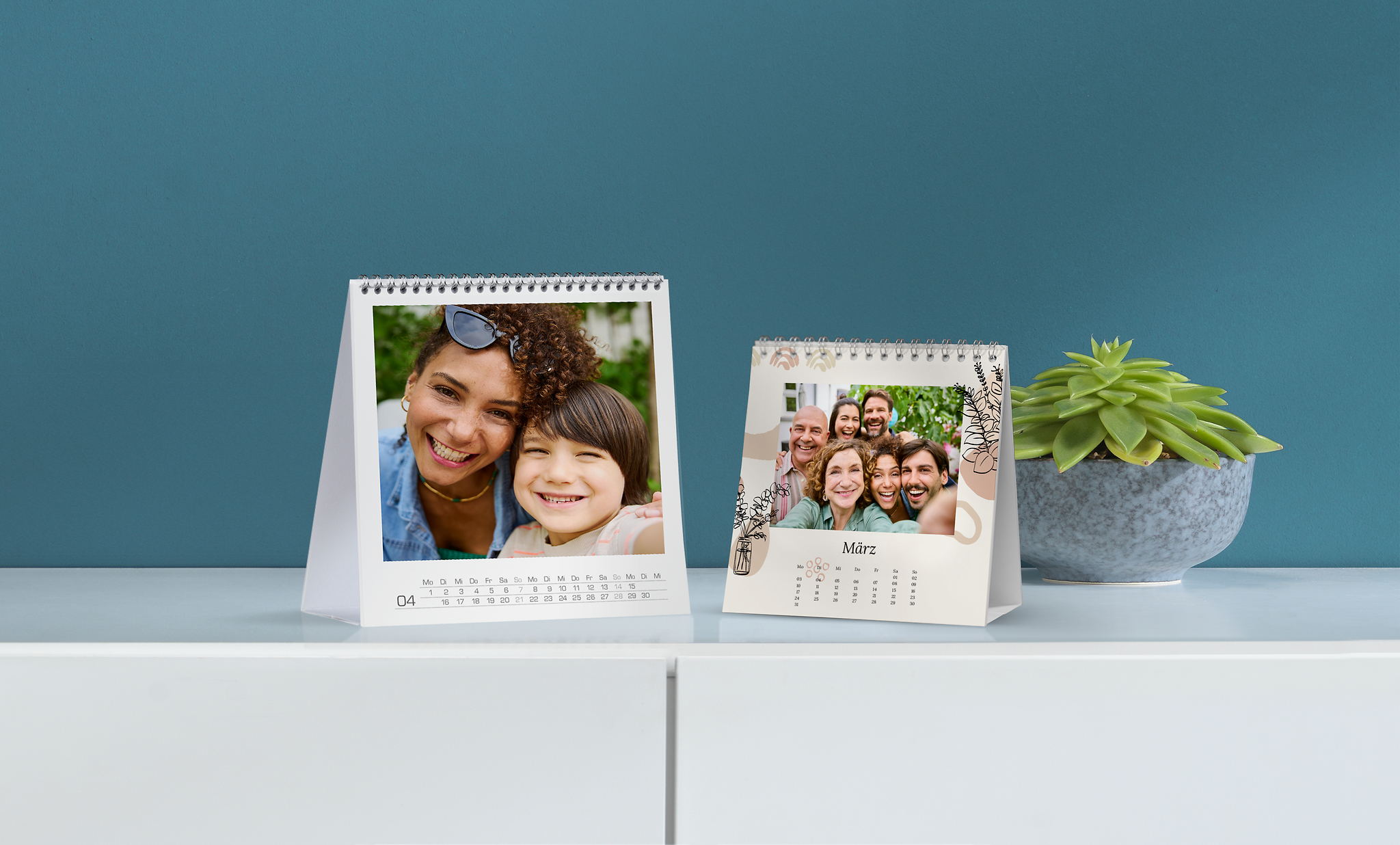 Hay dos calendarios de mesa sobre una cómoda. En los calendarios de mesa se ven fotos familiares. Uno de los calendarios tiene un diseño con dibujos negros de flores.